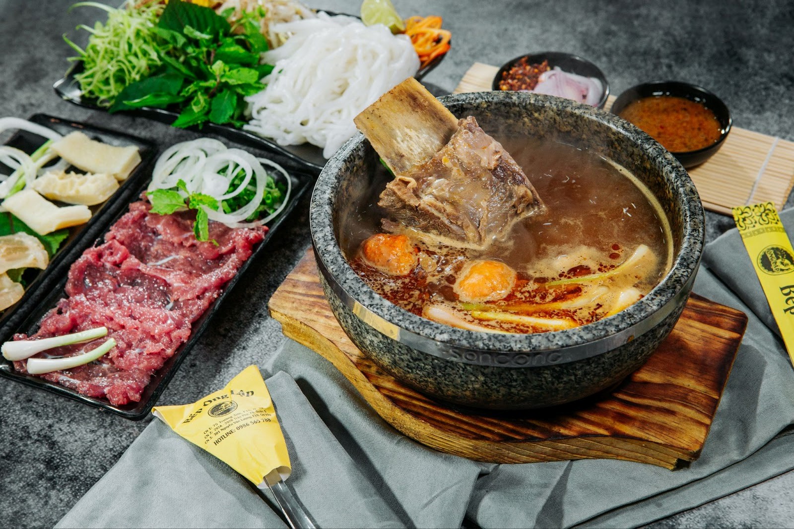 A bowl of soup with meat and vegetables on a wooden boardDescription automatically generated